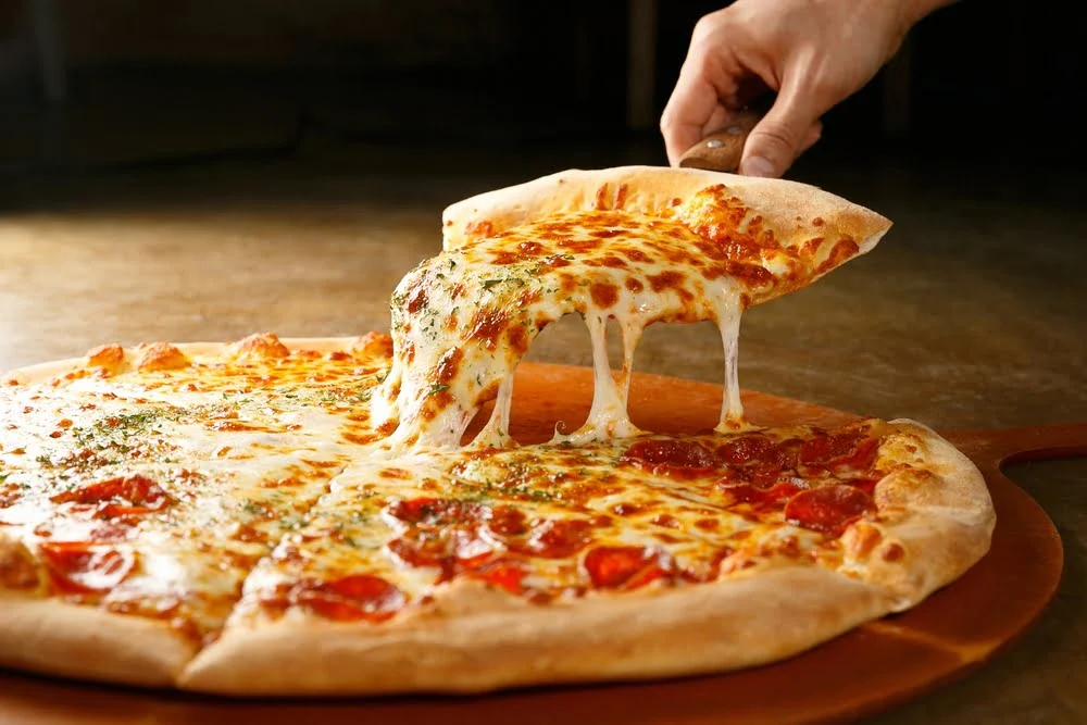 Fatia de pizza com queijo derretido a ser levantada, destacando textura, ingredientes e aspeto apetitoso de uma pizza acabada de sair do forno e que aumentou o consumo