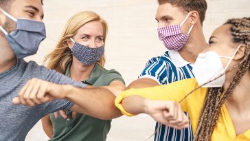 Young friends wearing face mask doing new social distancing greet with elbows bumps for preventing corona virus spread - Physical distance and friendship safety greetings concept