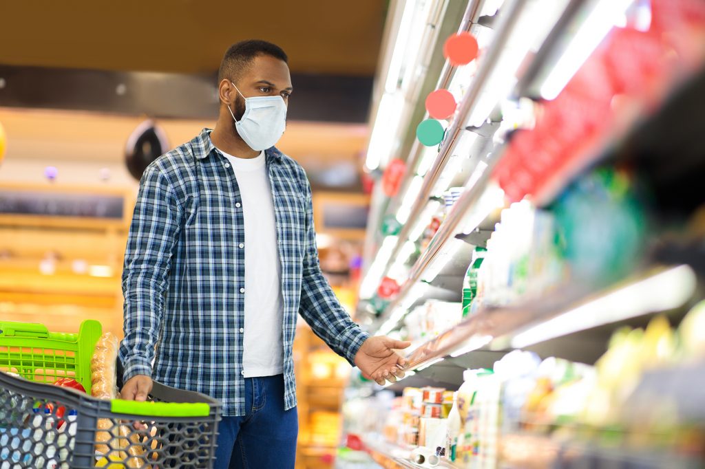 Panic Buying During Pandemic. Black Man Shopping In Supermarket Buying Food Wearing Face Mask, Guy Looking At Shelf Preparing For Coronavirus Quarantine Lockdown Standing In Grocery Store. Copy Space