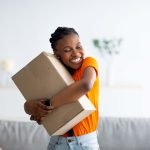Cheerful,Afro,Woman,Hugging,Carton,Parcel,,Receiving,Long,Awaited,Delivery,