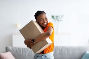 Cheerful,Afro,Woman,Hugging,Carton,Parcel,,Receiving,Long,Awaited,Delivery,
