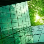 Eco-friendly building in the modern city. Green tree branches with leaves and sustainable glass building for reducing heat and carbon dioxide. Office building with green environment. Go green concept.