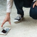 Person Picking Broken Smart Phone (Cracked Screen) of the Ground