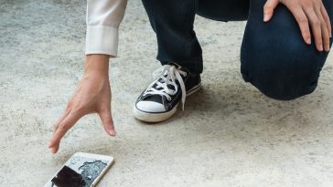 Person Picking Broken Smart Phone (Cracked Screen) of the Ground
