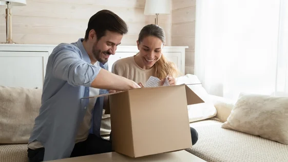Happy young couple unpacking awaited parcel at home together, curious man and woman looking into open cardboard box, satisfied customers received online store order, good delivery service