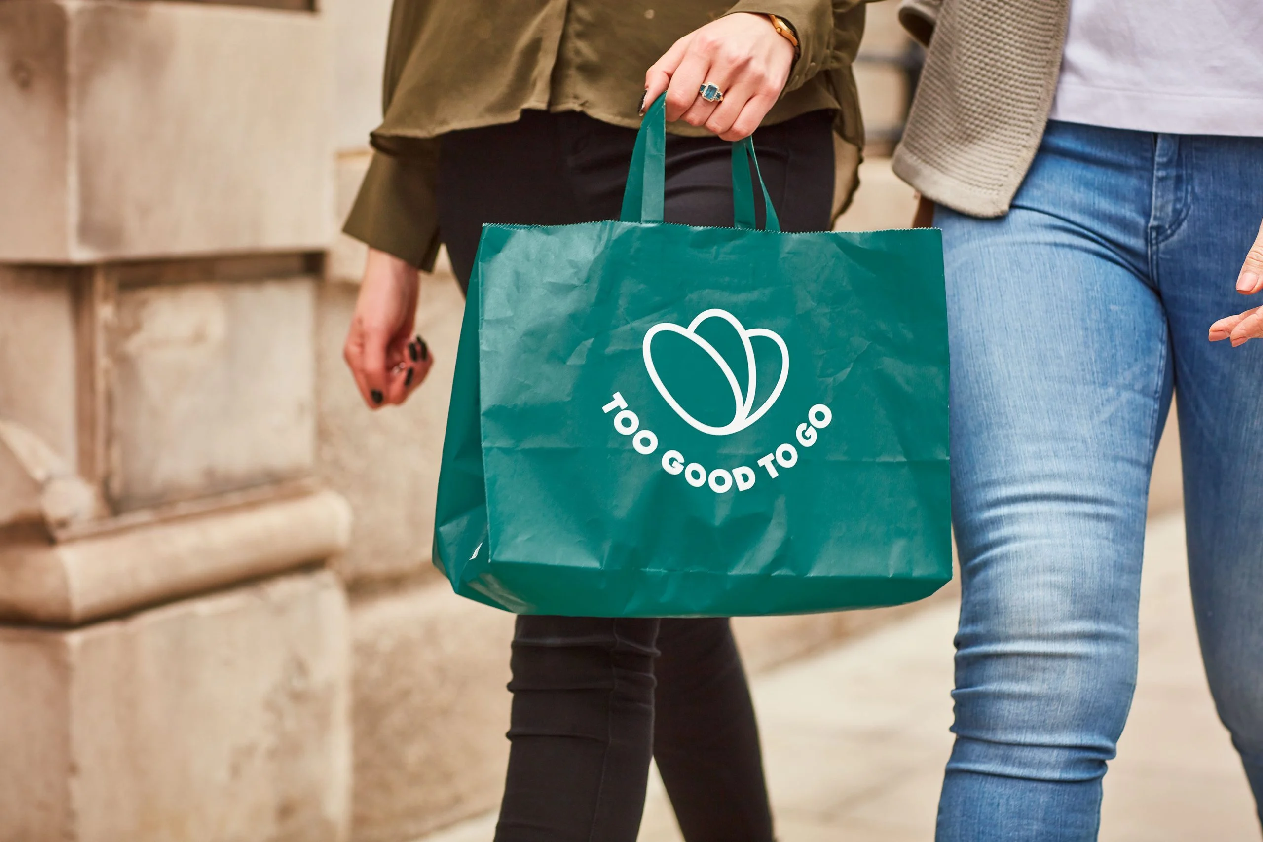 Pessoa a transportar saco reutilizável da Too Good To Go numa rua urbana, simbolizando combate ao desperdício alimentar e consumo sustentável