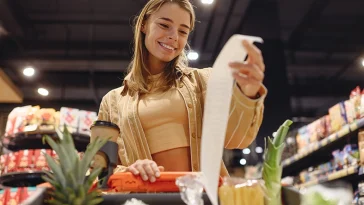 Young happy customer woman wears casual clothes read check bill shopping at supermaket store grocery shop buying with trolley cart choose products in hypermarket. Purchasing food gastronomy concept