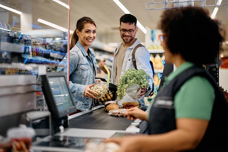 Happy couple talking to cahier while putting groceries on checkout counter in the supermarket.