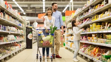 conceito de venda, consumismo e pessoas - família feliz com criança e carrinho de compras comprando comida em mercearia ou supermercado