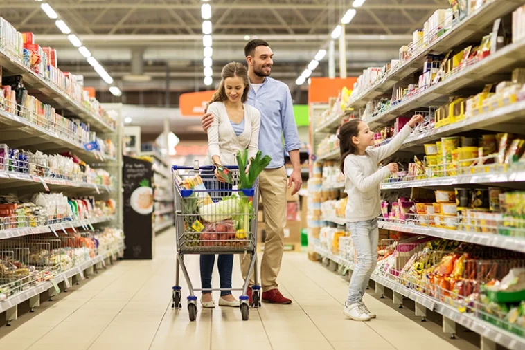 conceito de venda, consumismo e pessoas - família feliz com criança e carrinho de compras comprando comida em mercearia ou supermercado