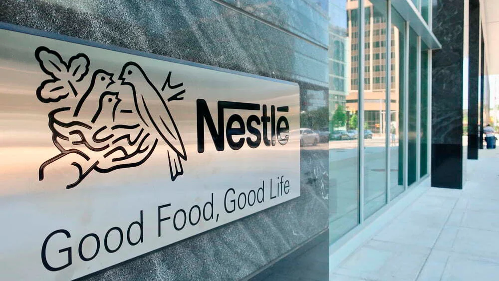Placa com o logótipo da Nestlé e o slogan ‘Good Food, Good Life’ na fachada de um edifício empresarial moderno