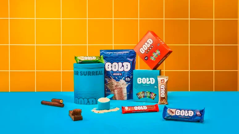 Gama de snacks proteicos Bold Snacks, incluindo barras e produtos whey, apresentada em cenário colorido com fundo laranja e azul