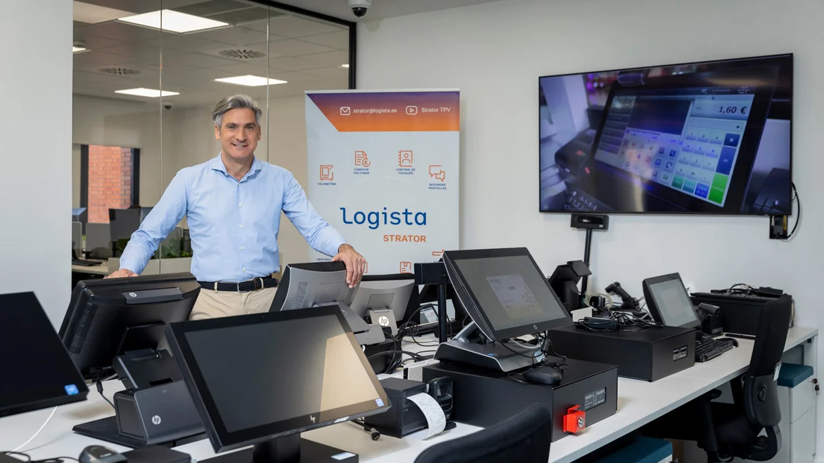 Homem em ambiente de escritório junto a equipamentos de ponto de venda (POS), com branding Logista Strator visível ao fundo