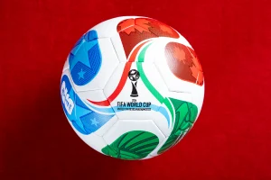 Bola oficial do Mundial 2026 com design colorido, apresentada sobre fundo vermelho