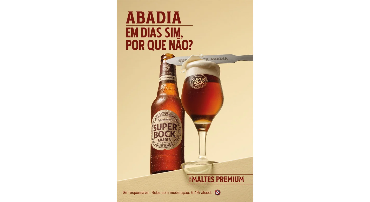 Garrafa e copo de Super Bock Abadia cerveja com espuma cremosa, numa campanha publicitária com a mensagem “Abadia, em dias sim, por que não?”