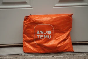 Encomenda da Temu em embalagem laranja colocada à porta de uma casa, representando entrega de compras online