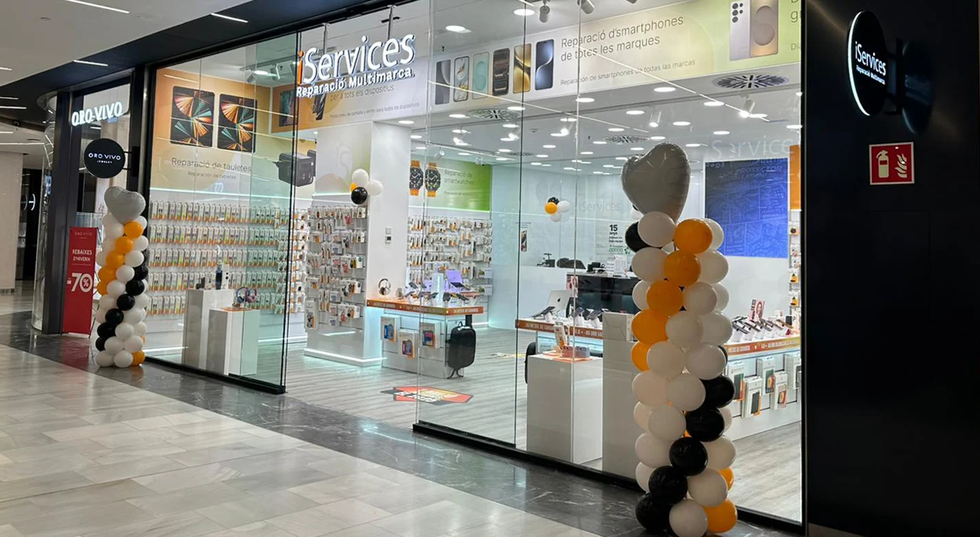 Loja iServices em centro comercial com fachada em vidro, exposição de acessórios para smartphones e balcão de reparação multimarca, decorada com balões laranja, branco e preto.