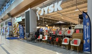 Loja da JYSK num centro comercial, em contexto de abertura. Comunicação de “Grande abertura”, exposição de mobiliário à entrada. Foco em preços promocionais