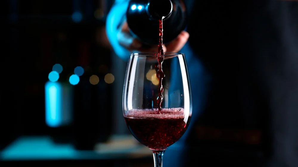 Vinho tinto a ser servido num copo em ambiente escuro e sofisticado, com foco no movimento do líquido e atmosfera premium, remetendo para degustação, enologia, restauração e experiência vínica