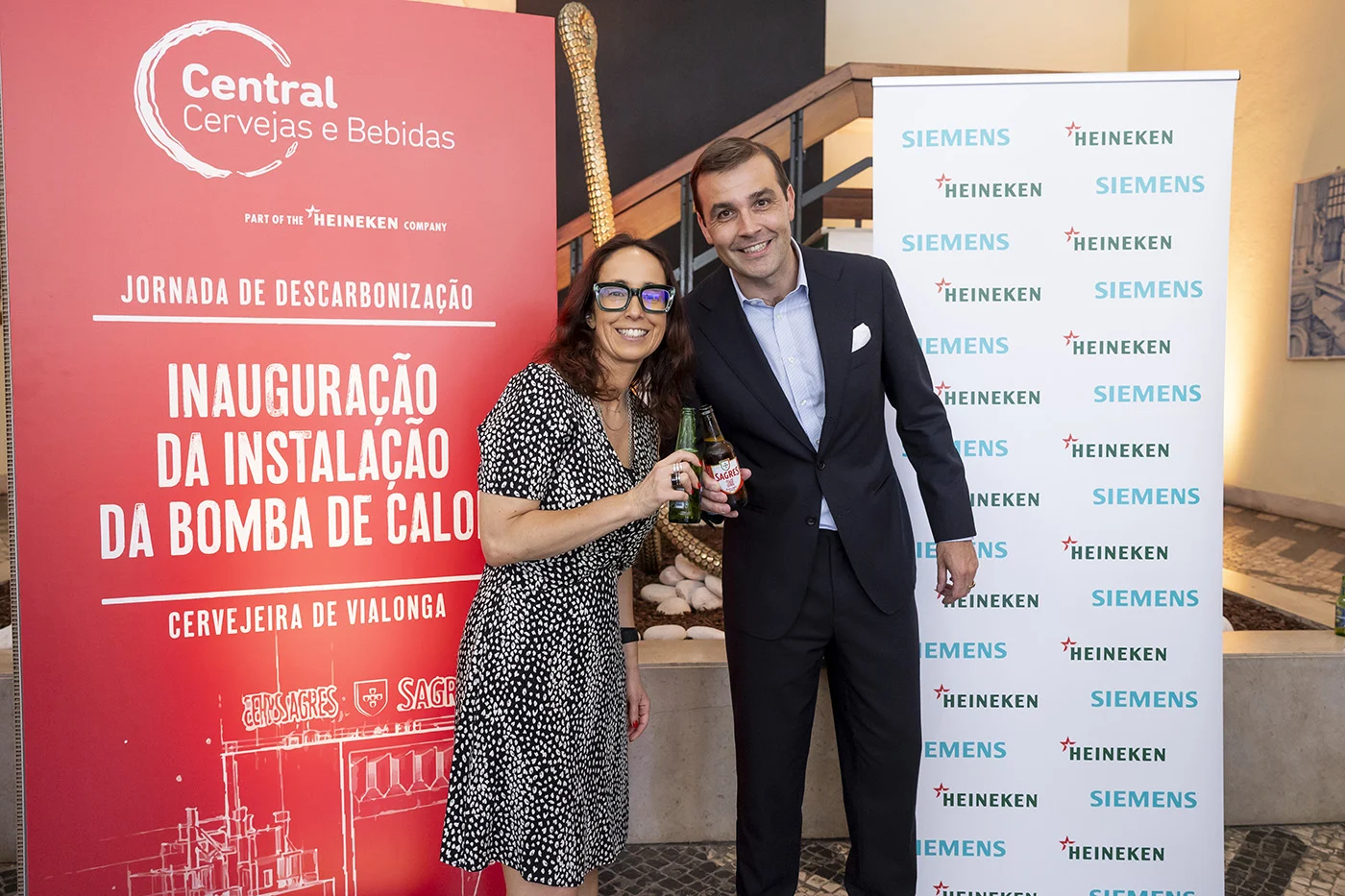 Dois convidados posam com garrafas numa inauguração da instalação da bomba de calor da Cervejeira de Vialonga