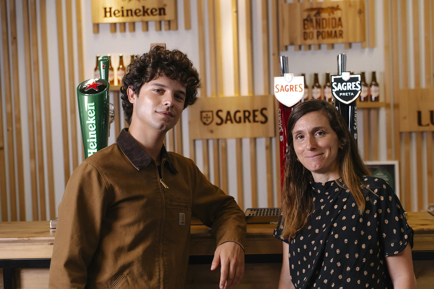 Duas pessoas em frente a torneiras de cerveja Heineken e Sagres
