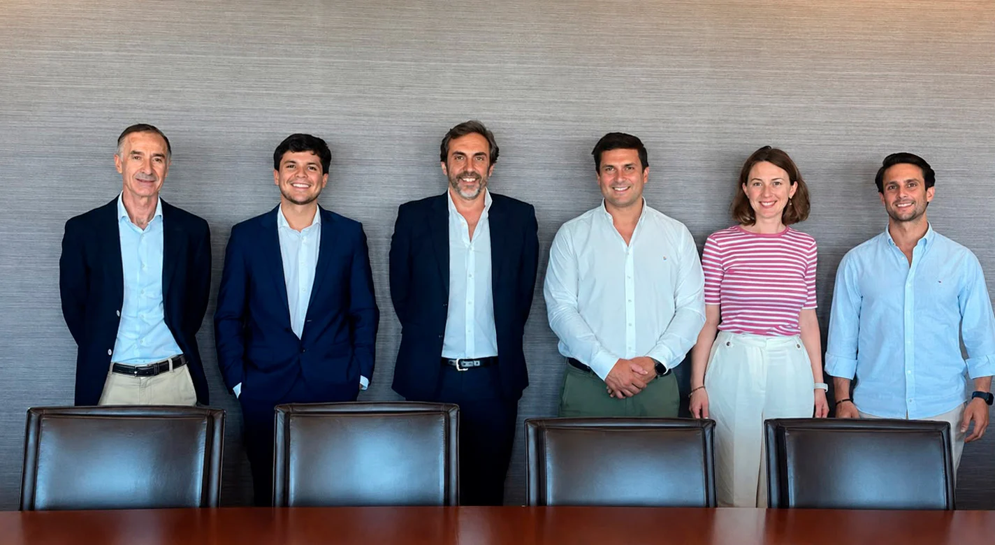 Seis pessoas em pé atrás de uma mesa de reunião, a sorrir para a câmara