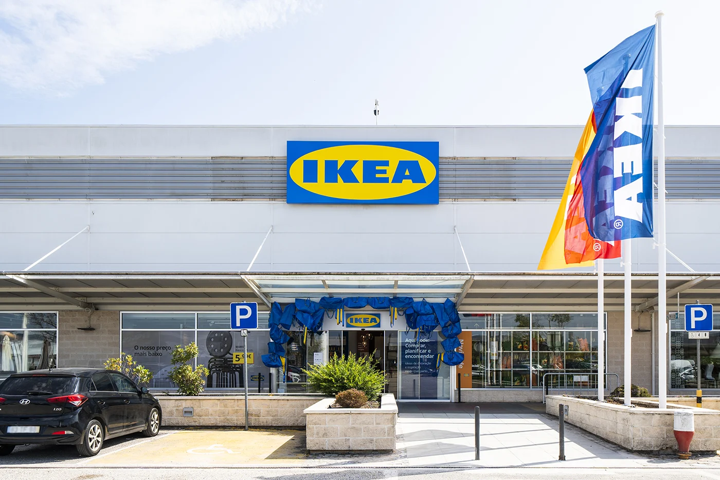Entrada de uma loja IKEA com estacionamento e bandeiras à frente