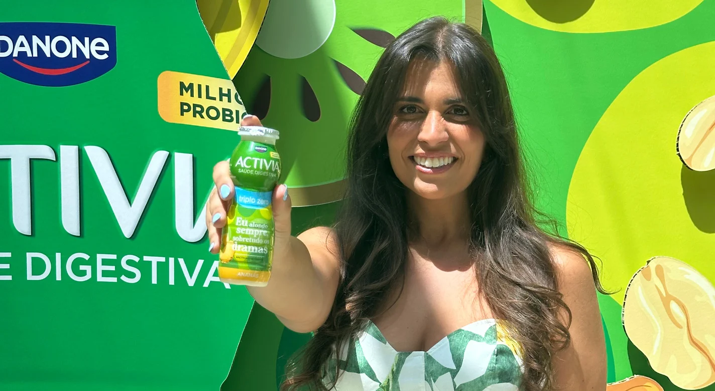 Mulher a sorrir a segurar uma garrafa de Activia diante de um painel verde da Danone