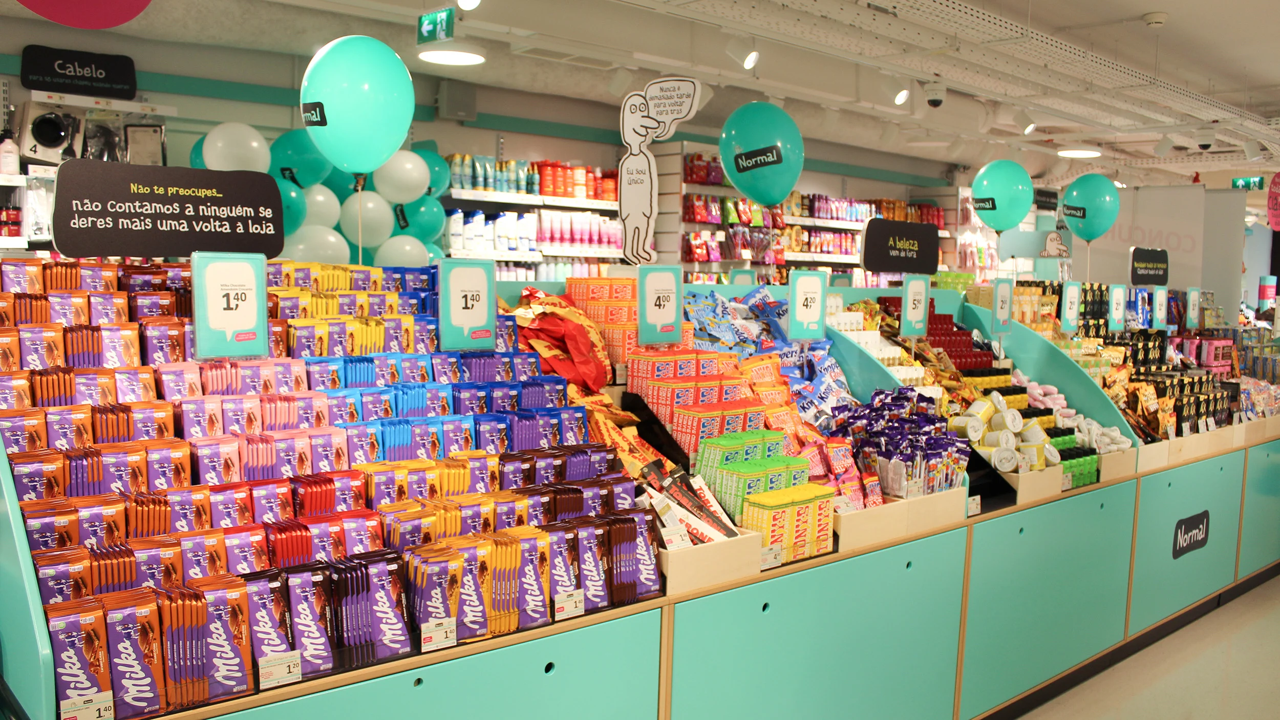 Interior de uma loja Normal com expositores repletos de chocolates, snacks e produtos de higiene e beleza