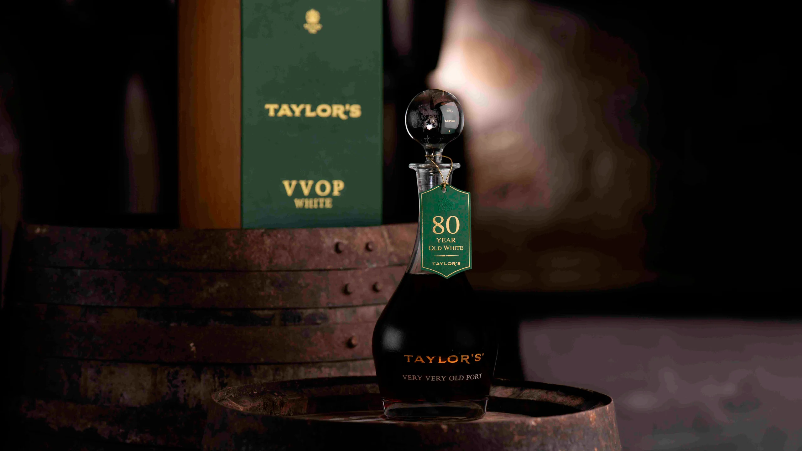 Garrafa de vinho do Porto Taylor’s Very Very Old Port, com 80 anos, apresentada sobre uma pipa de madeira em ambiente escuro
