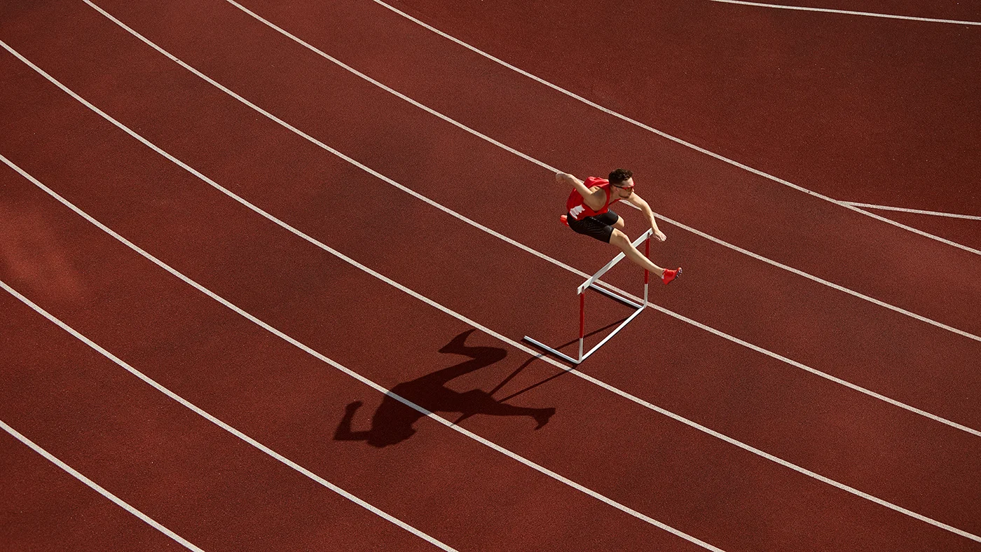 Atleta a saltar uma barreira numa pista de atletismo