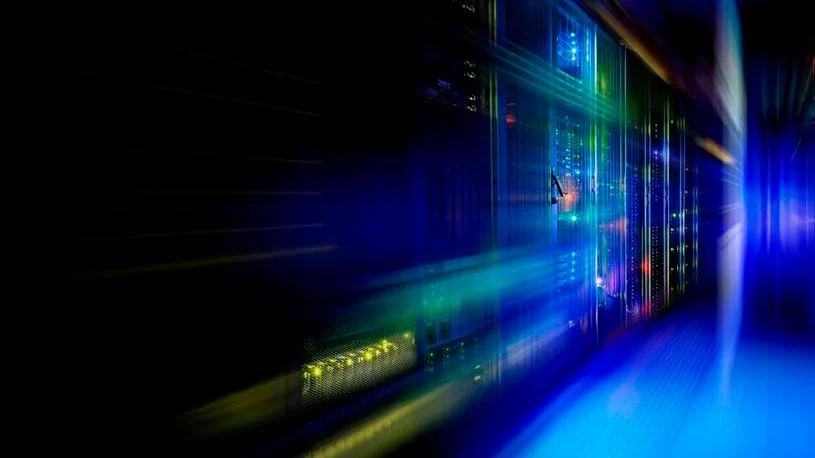 Servidores num centro de dados iluminados por luzes azuis e verdes, representando infraestruturas digitais e data centers