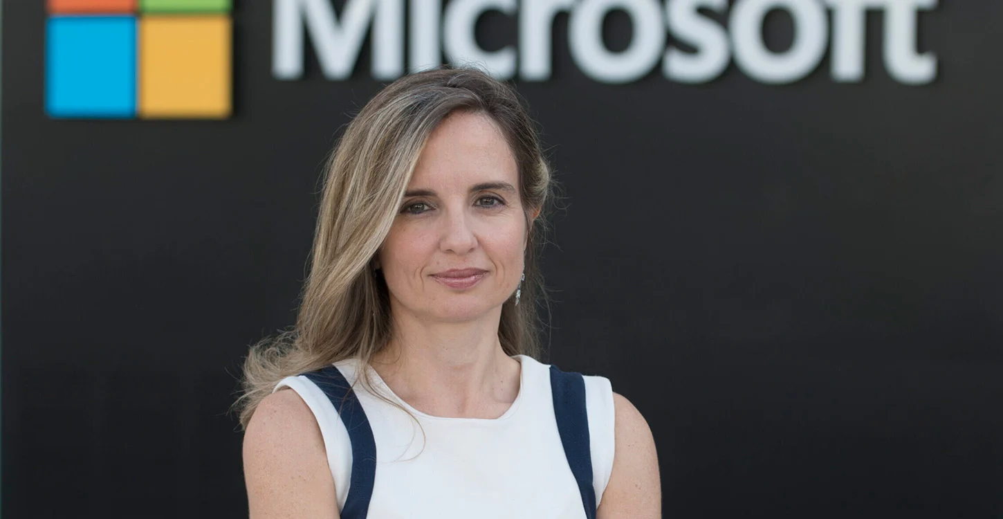 Mulher de cabelo comprido posa diante do logótipo da Microsoft