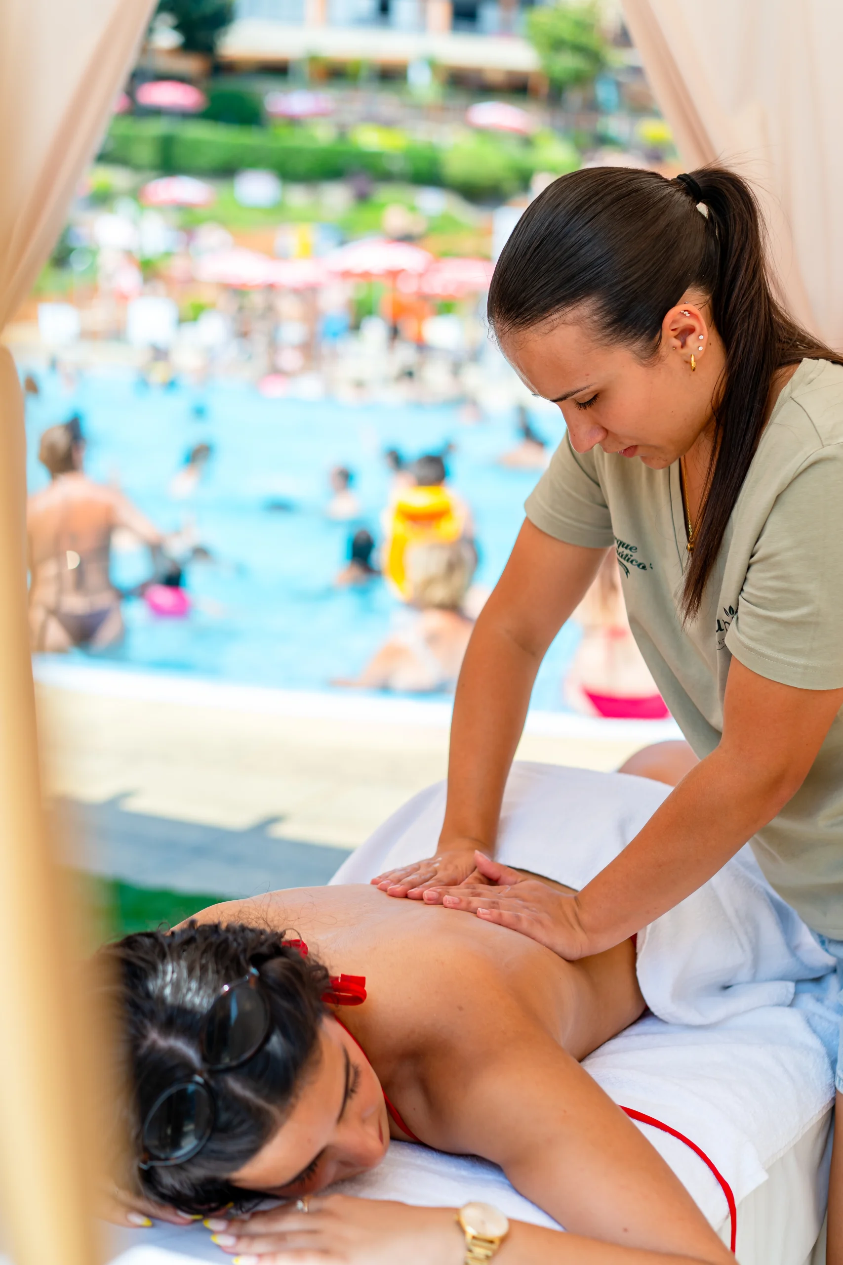 Massagem nas costas à beira da piscina, com uma terapeuta a aplicar pressão a uma cliente deitada