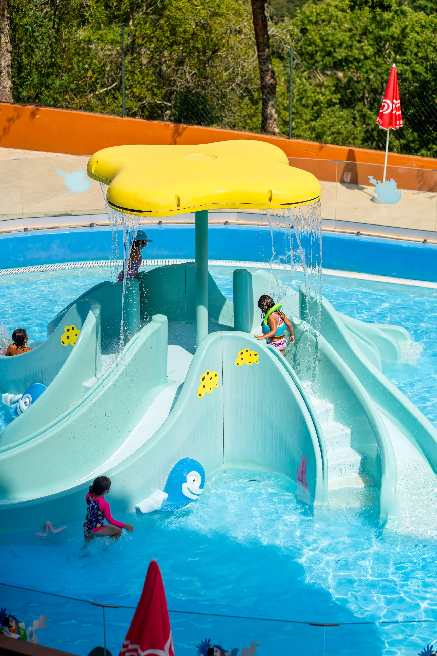 Crianças a brincar numa estrutura de água com escorregas e jatos num parque aquático infantil