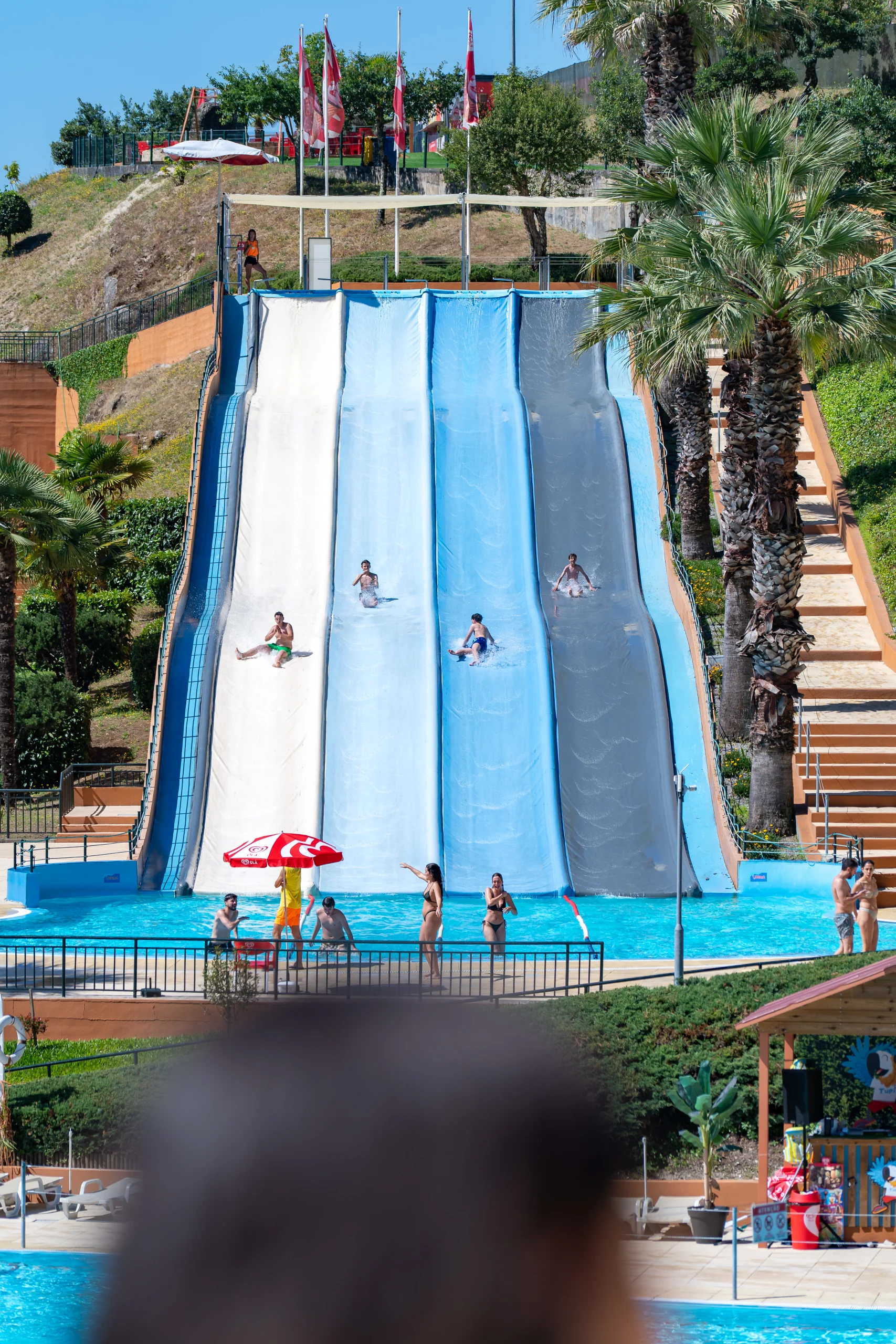 Escorrega aquático com quatro pistas e pessoas a descer para a piscina