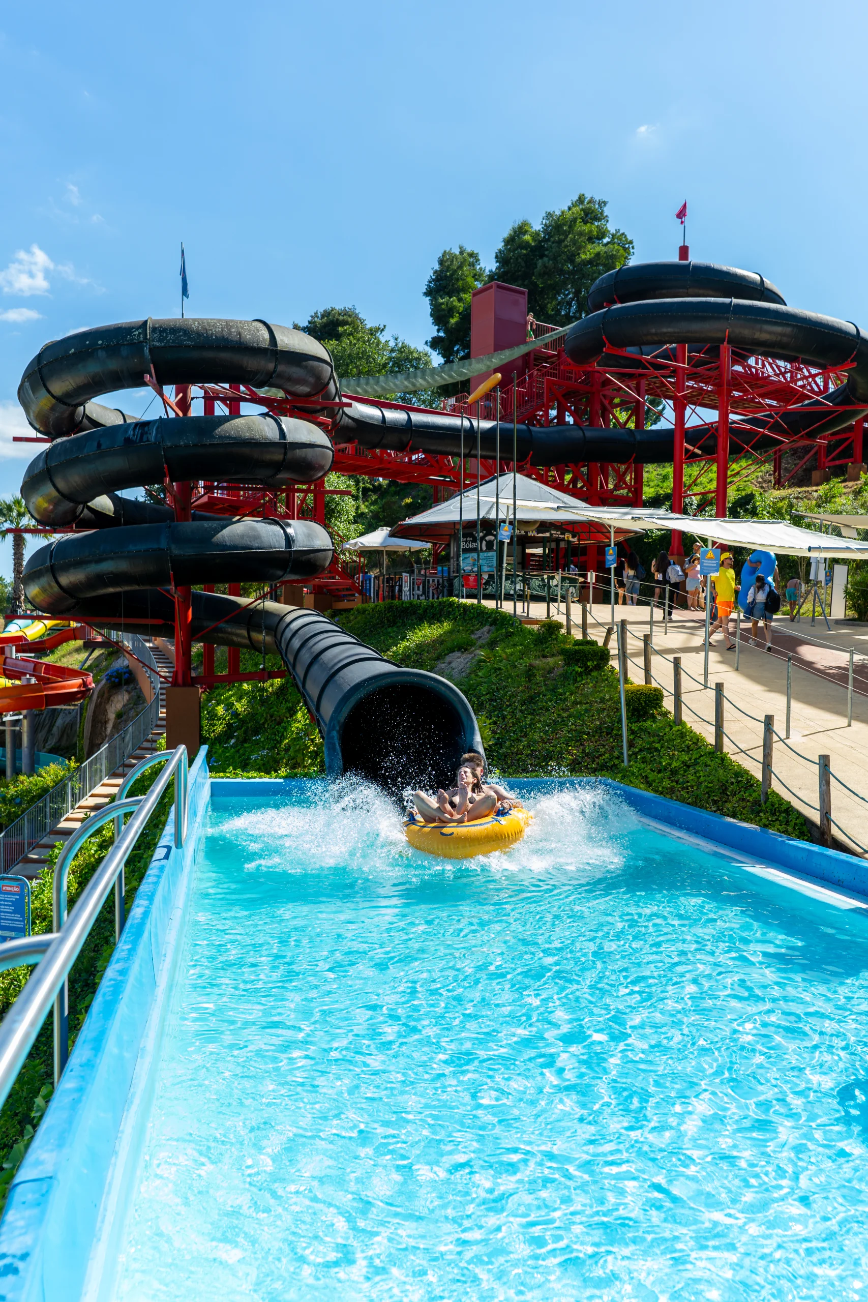 Toboágua num parque aquático, com pessoas a descer numa boia amarela e água a salpicar na piscina