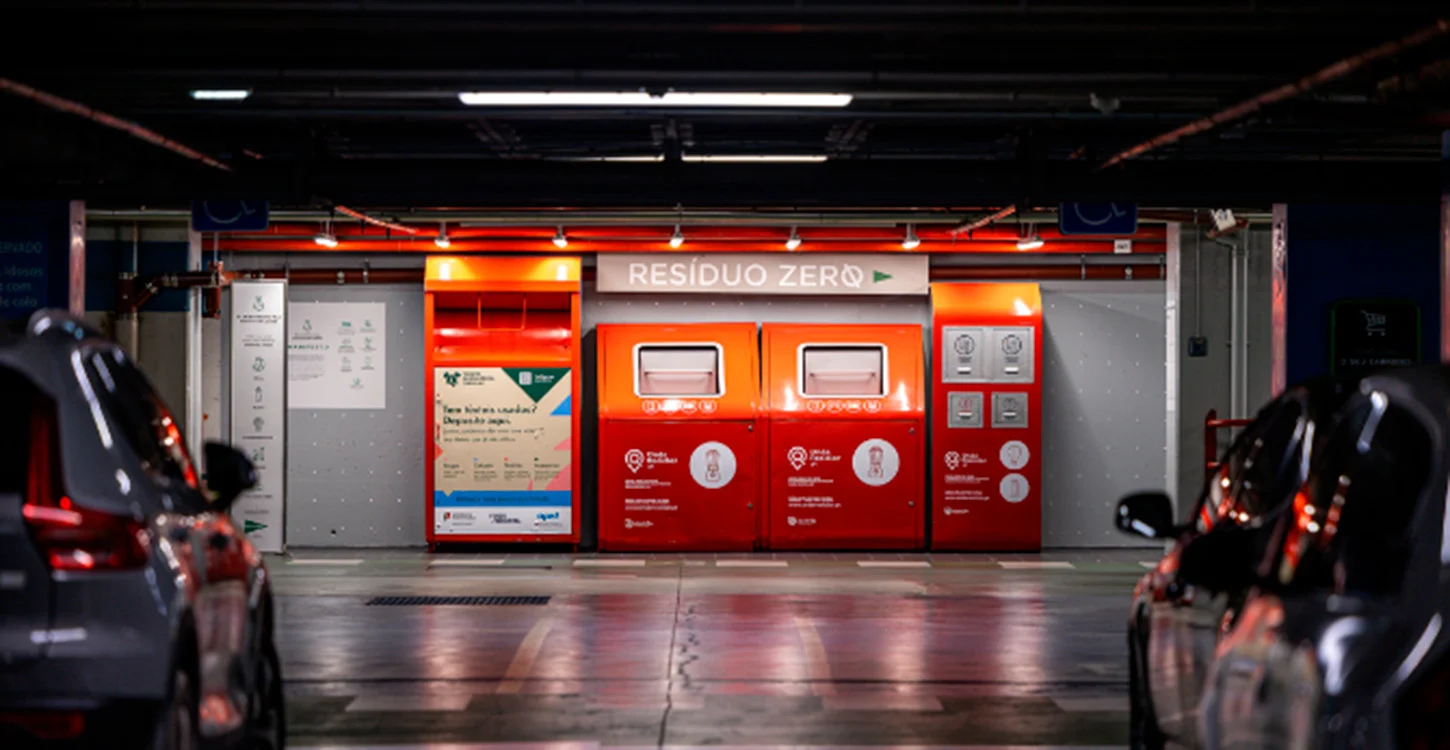 Ponto de recolha de resíduos com contentores para reciclagem e resíduos indiferenciados, entre carros estacionados