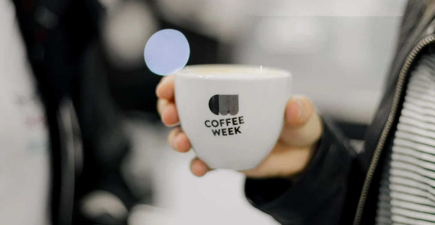 Pessoa a segurar uma chávena branca com a inscrição «COFFEE WEEK»