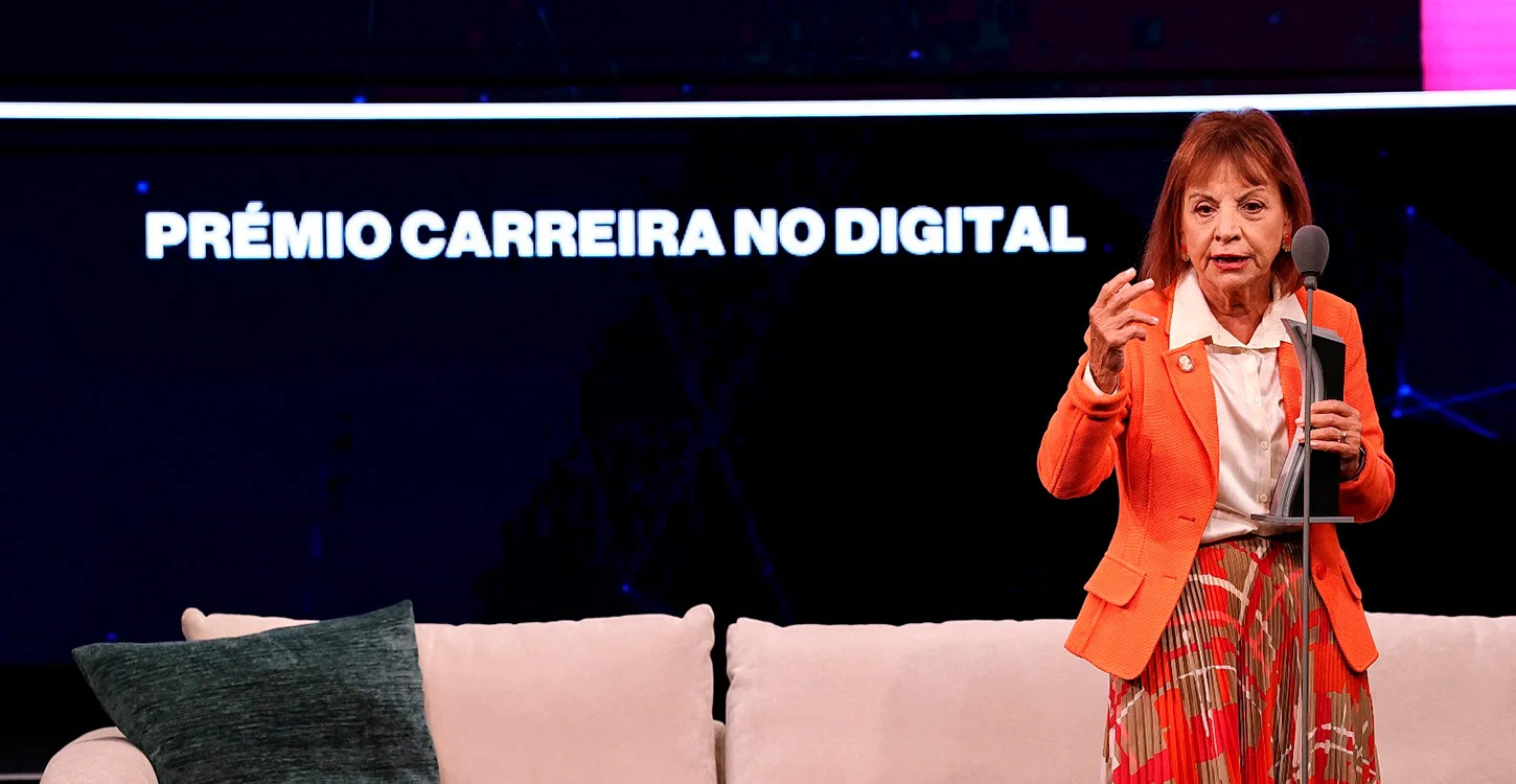 Mulher a receber um prémio no palco, com o texto “PRÉMIO CARREIRA NO DIGITAL” ao fundo