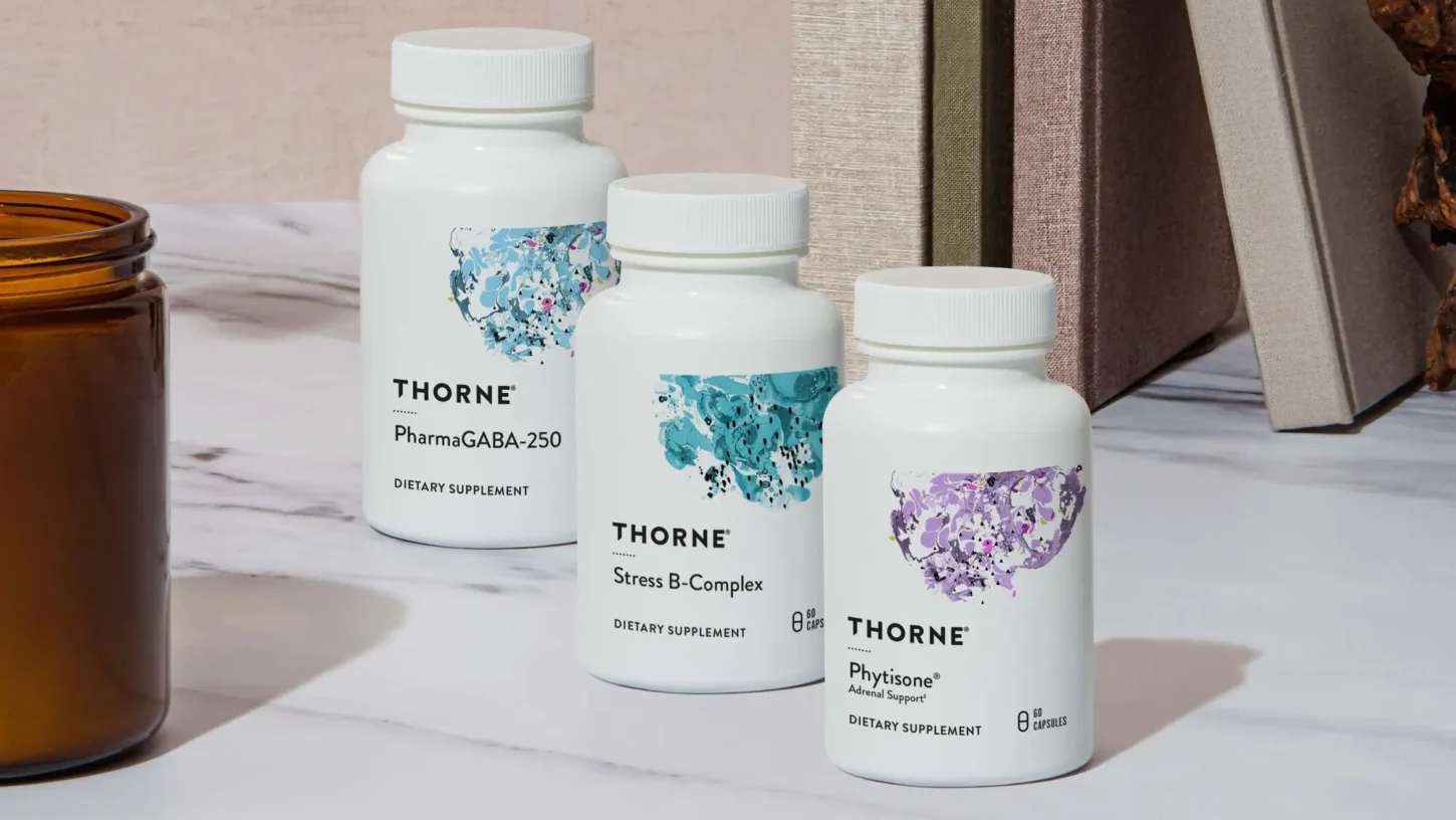 Três frascos de suplementos Thorne sobre uma superfície de mármore, com uma vela ao lado