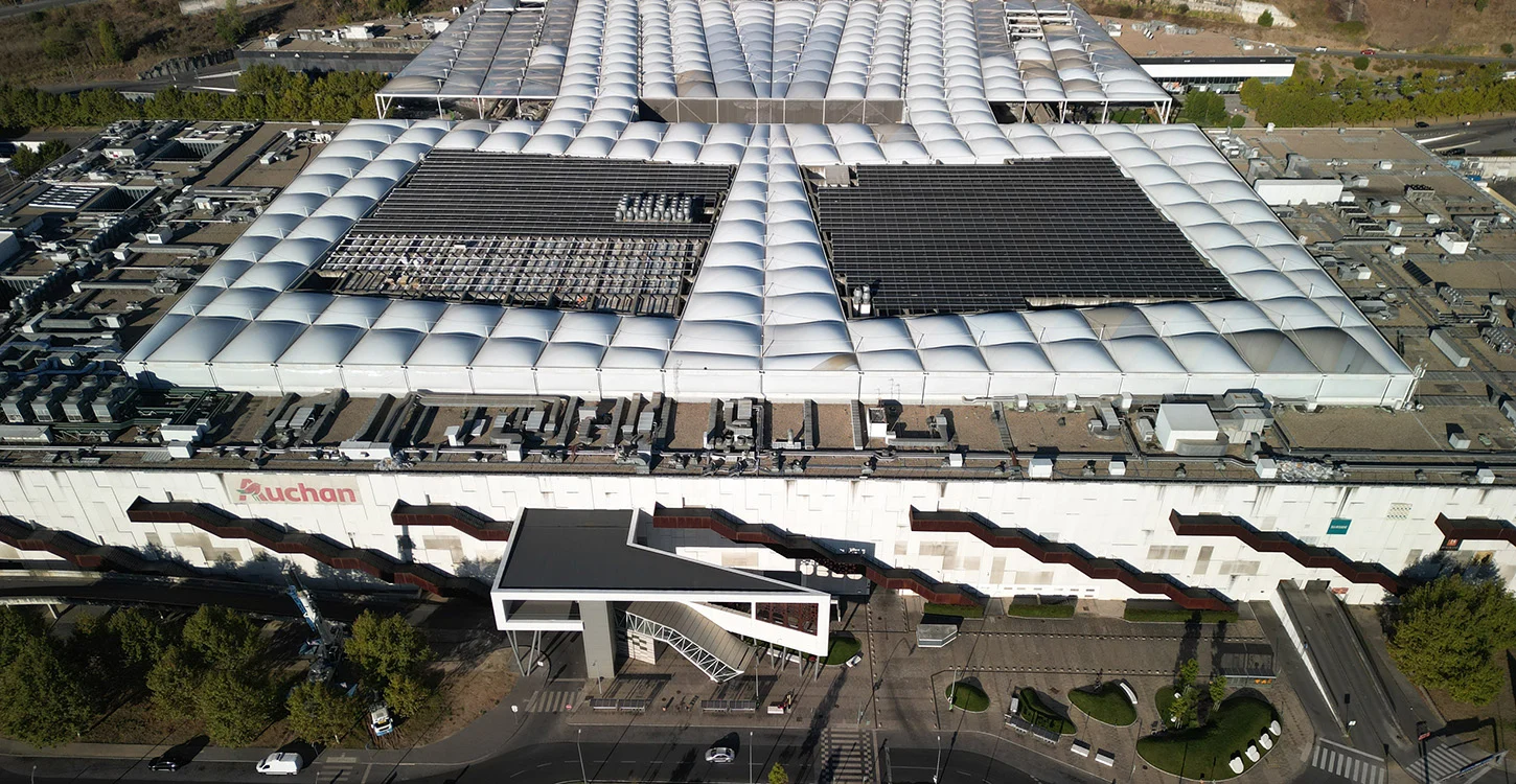 Vista aérea de um grande edifício comercial com o logótipo Auchan no exterior e painéis solares no telhado