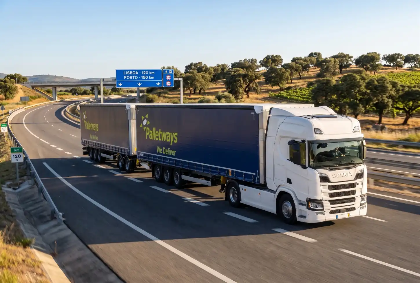 Camião de mercadorias numa autoestrada, com sinalização para Lisboa e Porto e sobreiros na paisagem