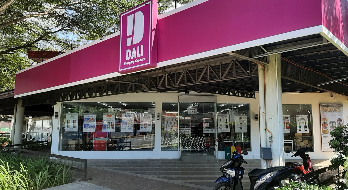 Entrada de uma mercearia DALI, com carrinhos de compras e motas estacionadas