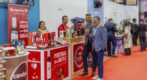 Stand da ginja Mariquinhas numa feira, com produtos expostos e três homens a brindar