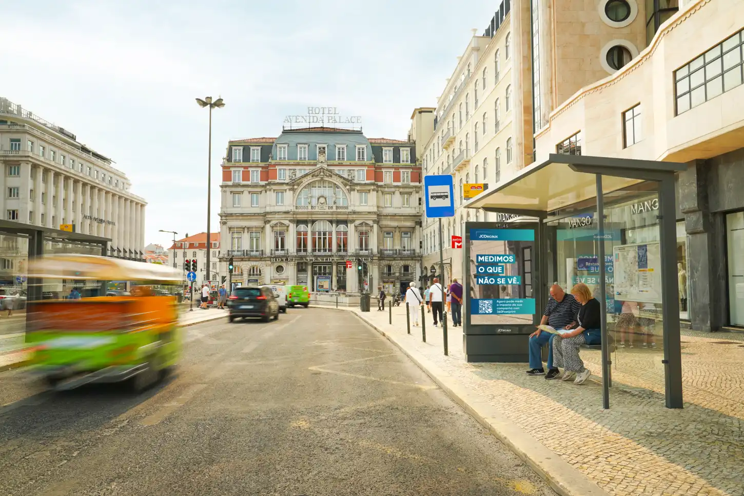 Rua urbana junto ao Hotel Avenida Palace, com um autocarro em movimento e uma paragem de autocarro