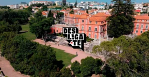 Vista aérea de um palácio cor-de-rosa rodeado por jardins, com o logótipo «Desliga-te» em primeiro plano