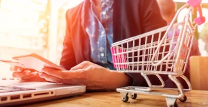 Pessoa a fazer compras online com um tablet, junto de um computador portátil e um carrinho de compras