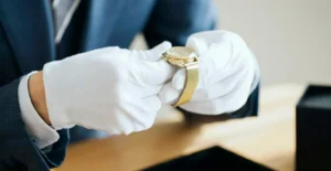 Mãos com luvas brancas a segurar um relógio de pulso dourado