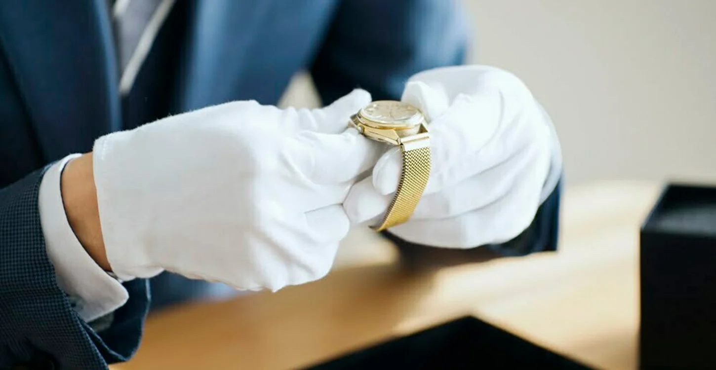 Mãos com luvas brancas a segurar um relógio de pulso dourado